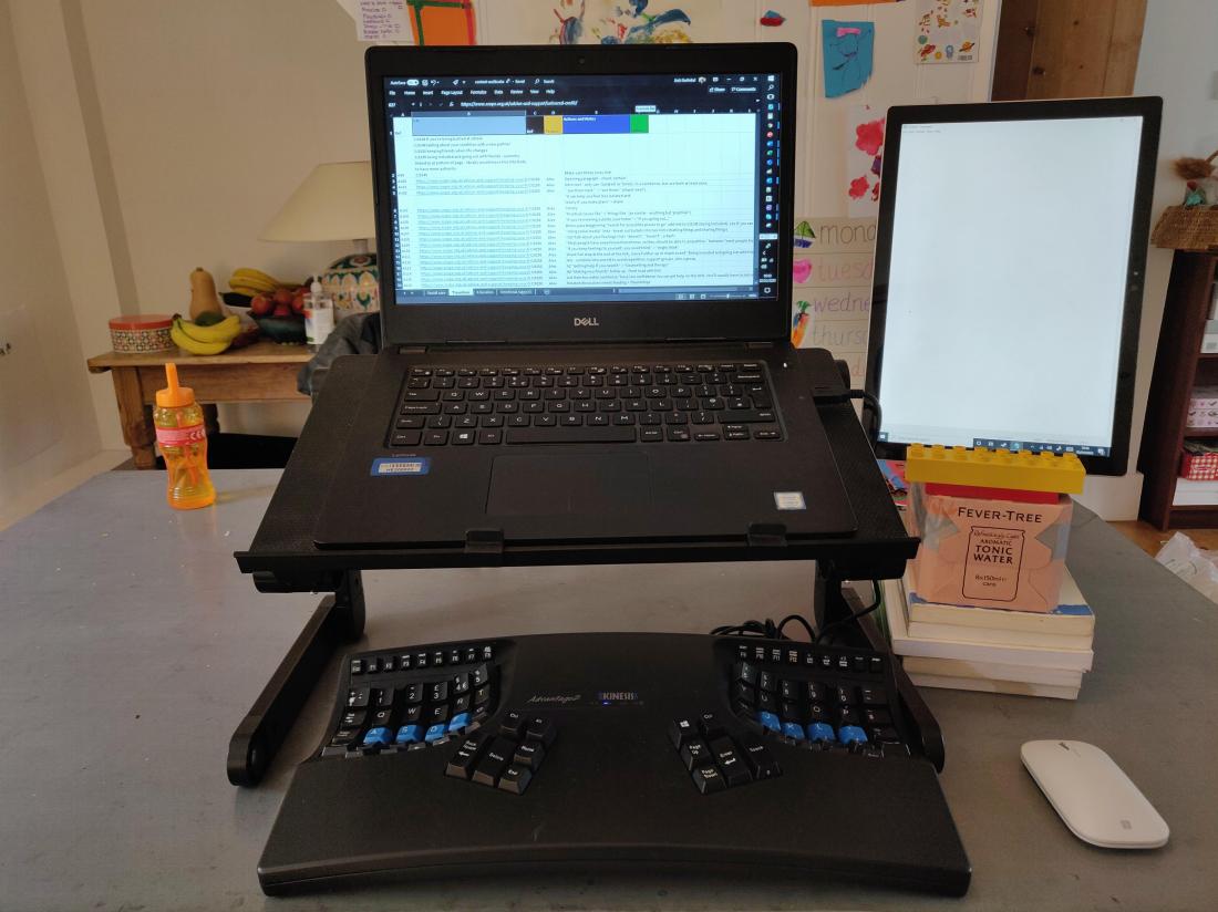 Laptop on stand connected to a tablet on a makeshift stand in portrait orientation. There is a wired keyboard and wireless mouse.