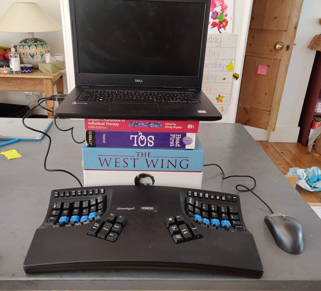 Laptop on top of a West Wing box set and some books. It's connected to a wired mouse and Kinesis Advantage 2 keybaord